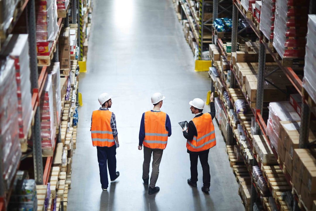 Warehouse racking and workers reviewing stored industrial supplies